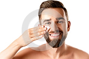 Young man is applying moisturizing and anti aging cream on his face