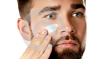 Young man is applying moisturizing and anti aging cream on his face