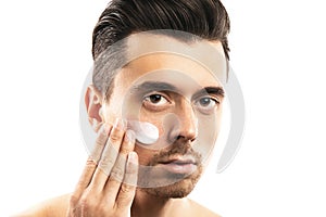 Young man is applying moisturizing cream on his face