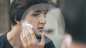 Young man applying shaving foam to his face in front of the mirror