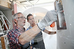 Young man apprentice with professional plasterer
