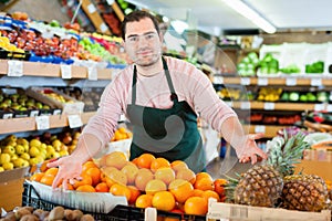 Young man in apron selling fresh oranges and fruits on the supermarket
