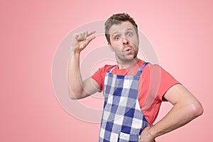 Young man in apron show small size by fingers demonstrate small measure