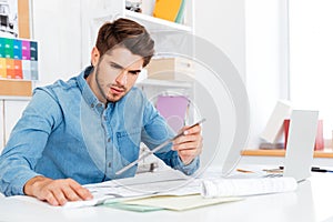 Young man architect holding ruler over diagram on the desk