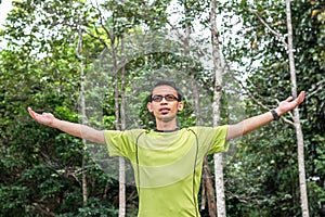 Young man arms raised enjoying the fresh air in green forest.