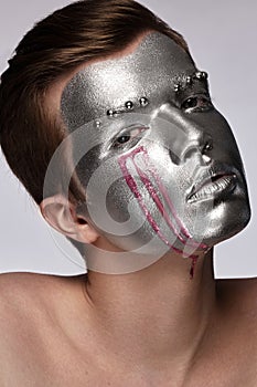 Young man with art creative art make-up with silver paint on his face.