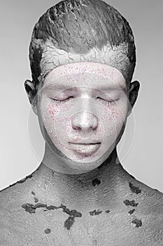 Young man with art creative make-up with mud on his face. Cosmetic mask.