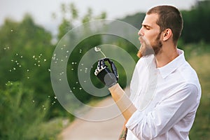 Young Man With Artificial limb is holding dandelion and blowing on it