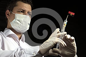 Young man as a doctor gives a medical injection to Angolan flag