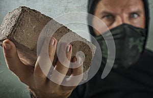 Young man as fanatic and aggressive anarchist rioter . furious and scary violent anti-system protester in face mask throwing brick