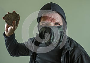 Young man as fanatic and aggressive anarchist rioter . furious and scary violent anti-system protester in face mask throwing stone photo