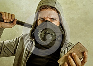 Young man as fanatic and aggressive ultra anarchist rioter . furious anti-system protester in face mask holding baton throwing photo