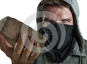 Young man as radical and aggressive anarchist rioter holding brick . furious anti-system protester in face mask throwing stone in