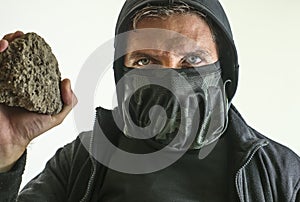 Young man as radical and aggressive anarchist rioter holding brick . furious anti-system protester in face mask throwing stone in