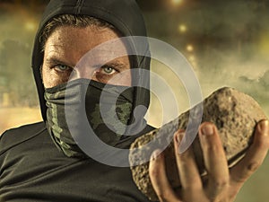 Young man as ultra and radical anarchist rioter . furious antifa protester in face mask throwing brick hostile on street on