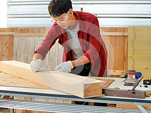 Young man Asian carpenter with red shirt  in workshop store working on wood plank and measurement tools