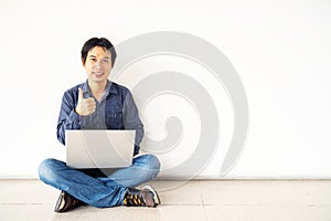 Young man asian sitting on the floor with using computer laptop happy with big smile doing ok sign, thumb up with fingers,