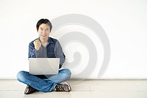 Young man asian sitting on the floor with using computer laptop happy excited with big smile posing isolated over white wall