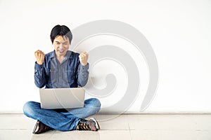 Young man asian sitting on the floor with using computer laptop happy excited with big smile posing isolated over white wall