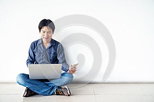 Young man asian sitting on the floor with using computer laptop and mobile phone is happy excited with big smile posing isolated