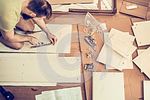 Young man assembles furniture in the new house, the details laid around him on the floor photo