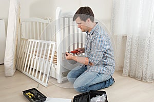 Young man assembling baby`s crib in nursery