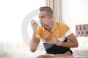 Young man with asthma inhaler on bed