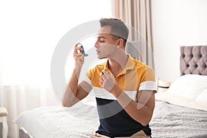 Young man with asthma inhaler on bed