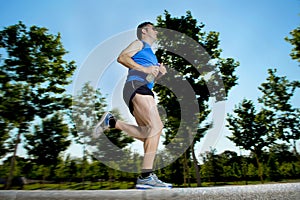 Young man with athletic runner legs holding isotonic energy drink while running in city park