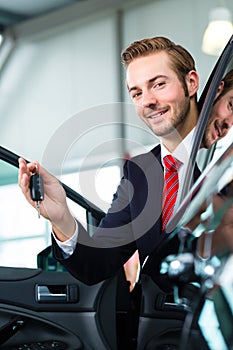 Young man or auto dealer in car dealership