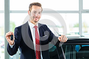 Young man or auto dealer in car dealership