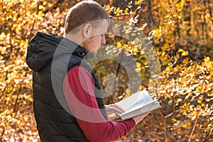 Young man in the autumn forest and reading book. Mental recreation in nature. Quiet country life. Escapism. Digital