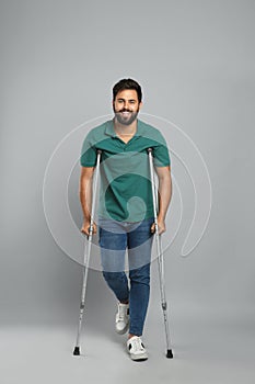Young man with axillary crutches on grey background photo