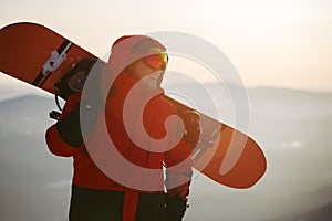 A young man on the background of the sunset sky with a snowboard