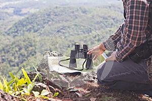 Young man with backpack and holding a binoculars sitting on top of mountain, Hiking and tourism concepts