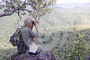 Young man with backpack and holding a binoculars sitting on top of mountain, Hiking and tourism concepts