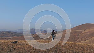 A young man with a backpack and photo equipment takes pictures of the mountain landscape from the top of the hill next