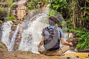 Young man with backpack standing near a waterfall in forest. Male hiker in the nature