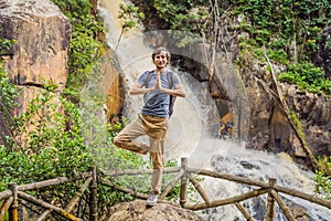 Young man with backpack standing near a waterfall in forest. Male hiker in the nature