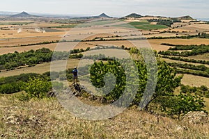 Young man with backpack standing on rock and looking to Czech central mountain valley