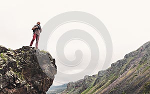 Young Man With Backpack Standing On Rocky Stone In Summer Mountains And Looking Into The Distance. Wanderlust Travel Concept