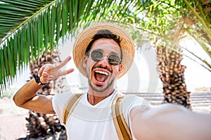 Young man with backpack taking selfie portrait on exotic beach -Smiling happy guy enjoying summer holidays