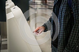 Young man with backpack touching interactive display using self service machine, doing self-check-in for flight or
