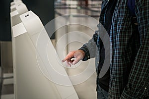 Young man with backpack touching interactive display using self service machine, doing self-check-in for flight or photo