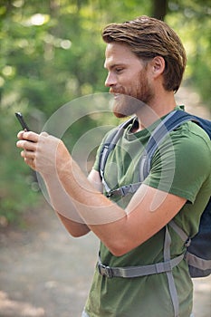 young man with backpack using smart phone in nature