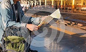 Young man backpacker waiting for train and travel bag and travel map.