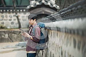 Young man backpacking in Korea. sitting in a Korean traditional house and using a tablet computer.