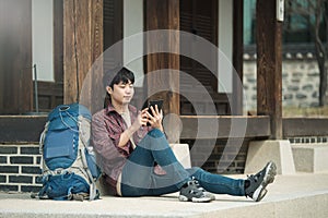 young man backpacking in Korea. sitting in a Korean traditional house and using a tablet computer.