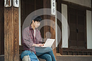 Young man backpacking in Korea. using a laptop sitting in a Korean traditional house.