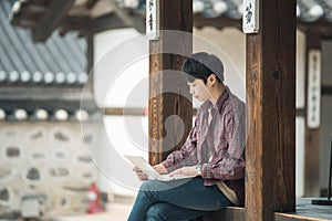 Young man backpacking in Korea. using a laptop sitting in a Korean traditional house.